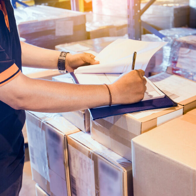 Warehouse worker writing on clipboard his checking details shipm